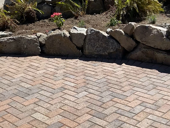 Paver patio adjacent to multi-tiered landscaped rockery retaining wall.