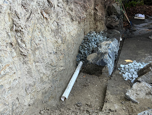 Drainage rocks and pipes installed behind retaining wall